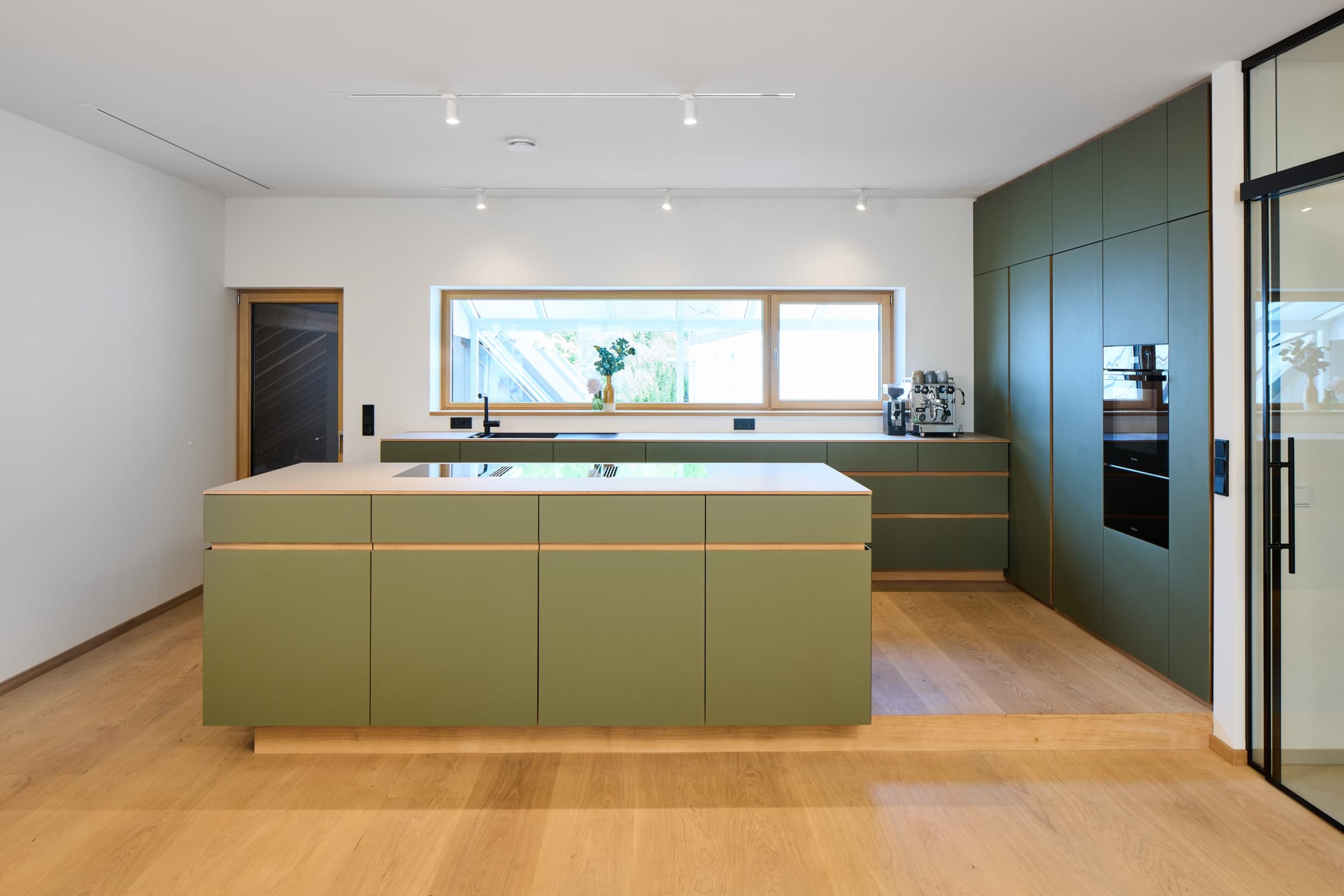grüne Küche mit großer Kochinsel vor einem großen Fenster