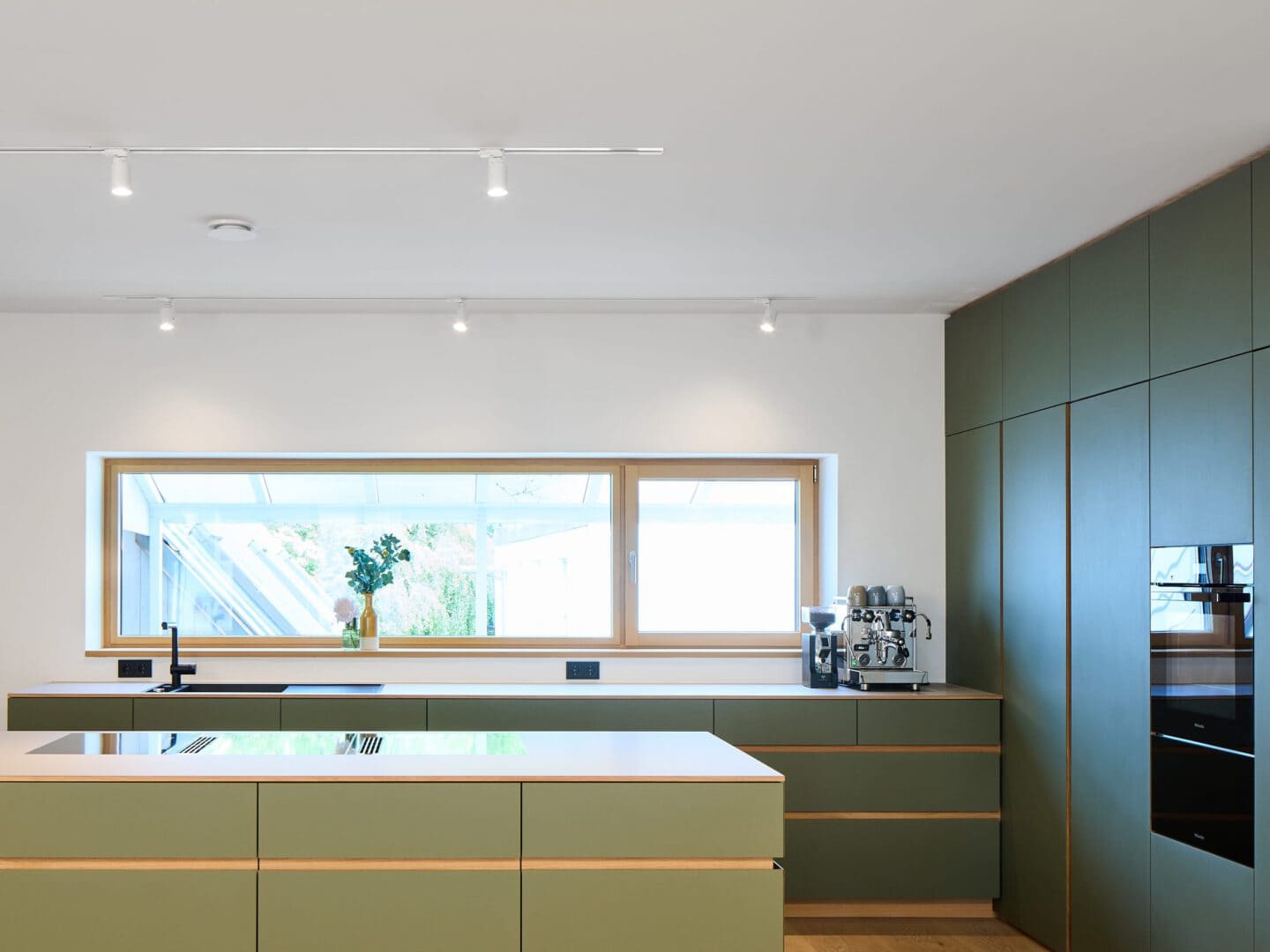 grüne Küche mit Kochinsel vor großem Fenster