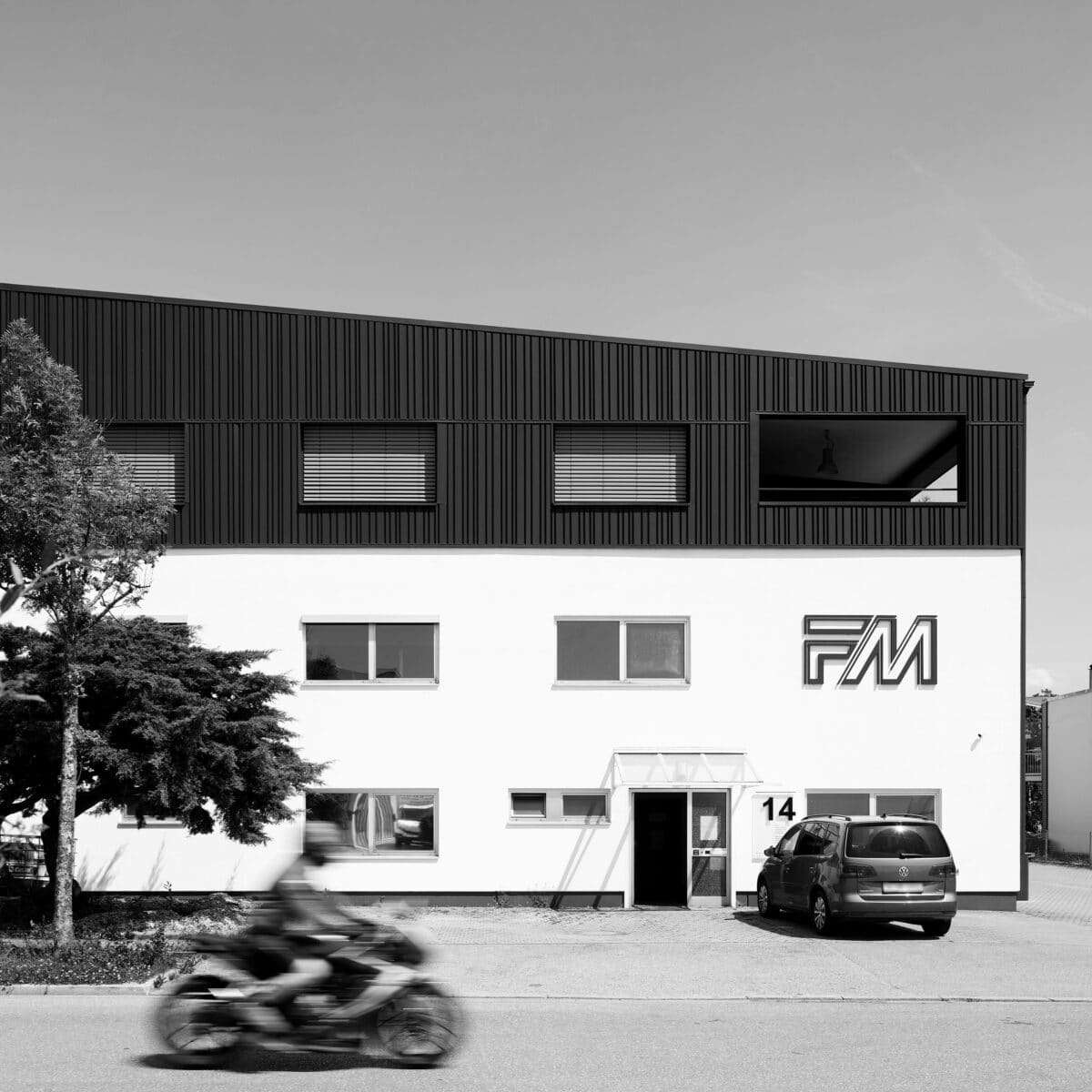 schwarz weiß Aufnahme eines weißen Firmengebäudes mit grauer Holzaufstockung