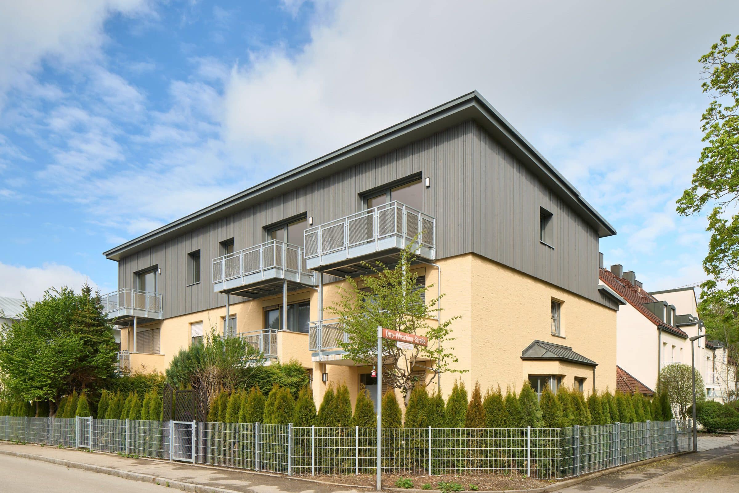gelbes Mehrparteienhaus mit grauer Holzaufstockung
