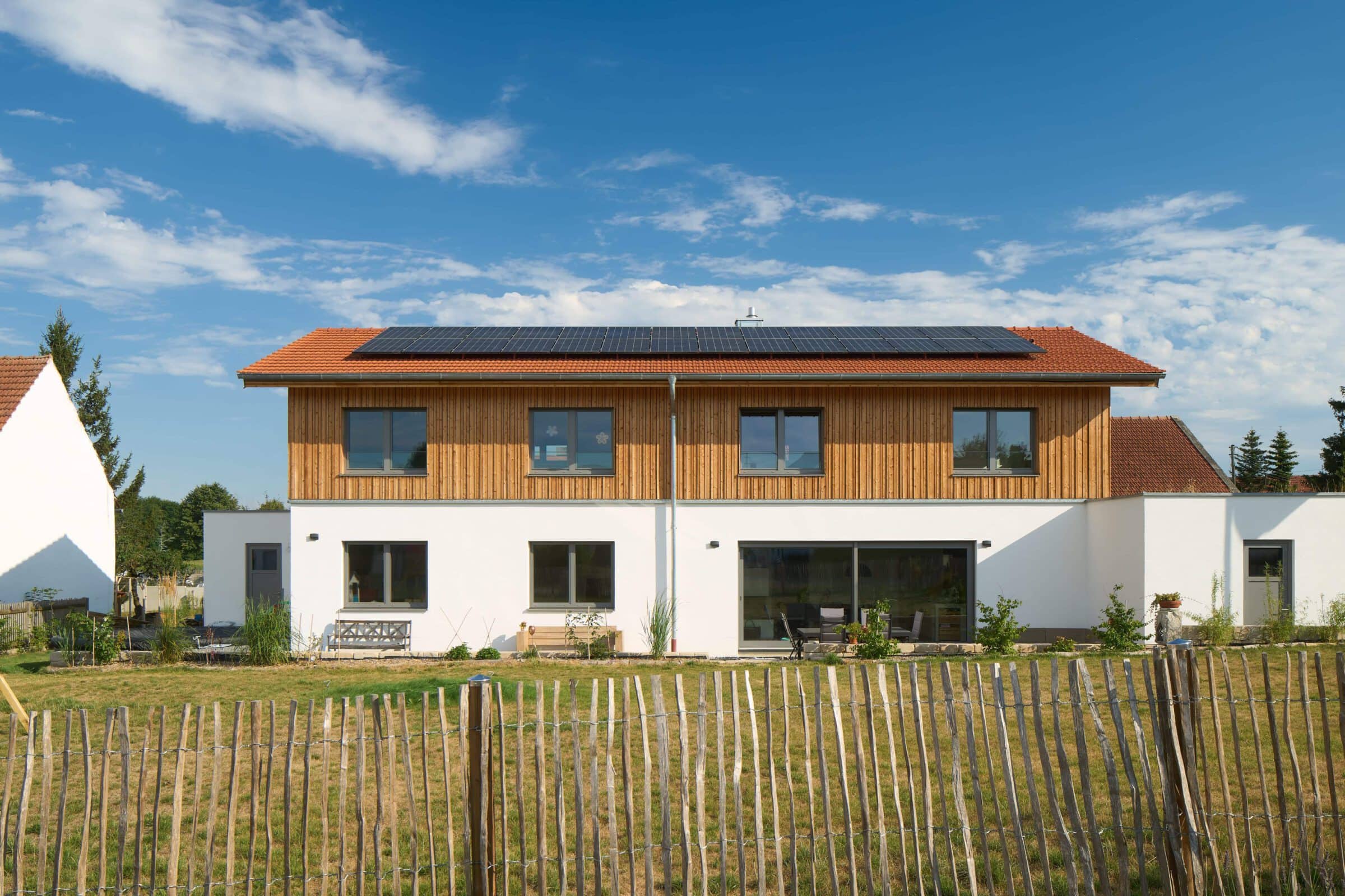 großes Einfamilienhaus mit Putz- Lärchenholfassade und einem Gartenzaun aus Holz