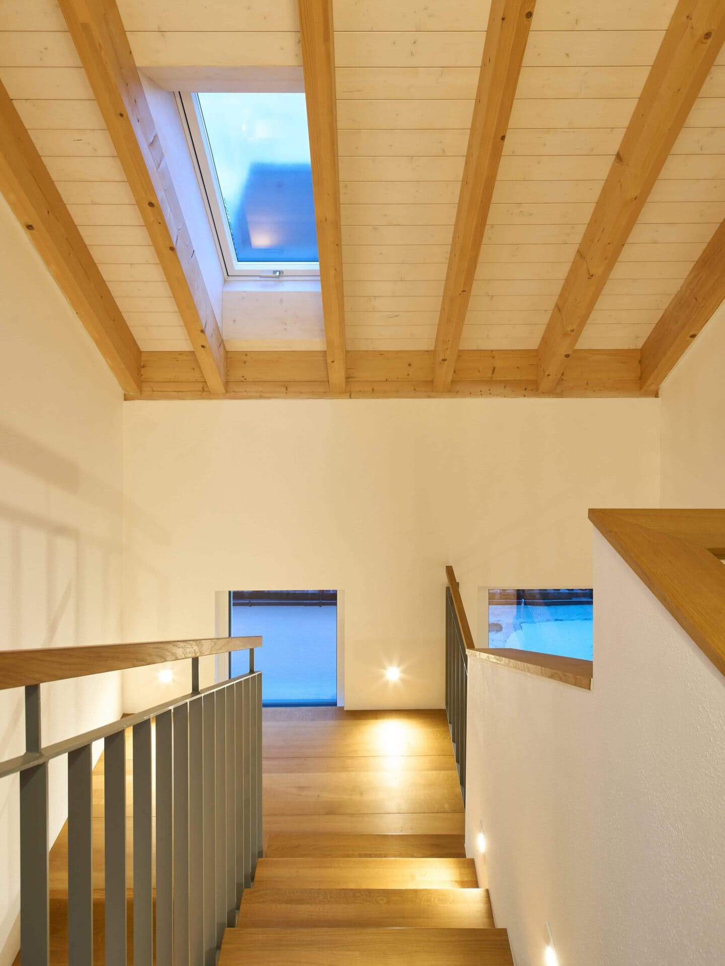 Blick ins Treppenhaus eines Doppelhauses mit Holztreppe und offenliegenden Dachbalken
