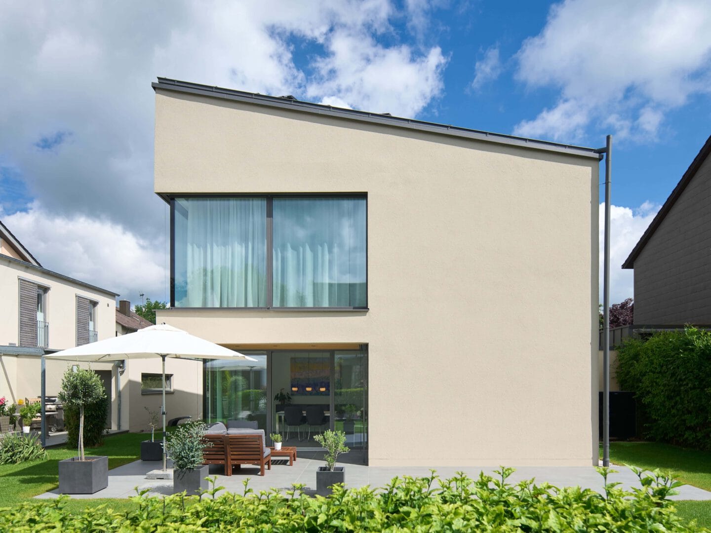Terrasse eines modernen Einfamilienhauses mit großen Fenstern und gepflegtem Garten.