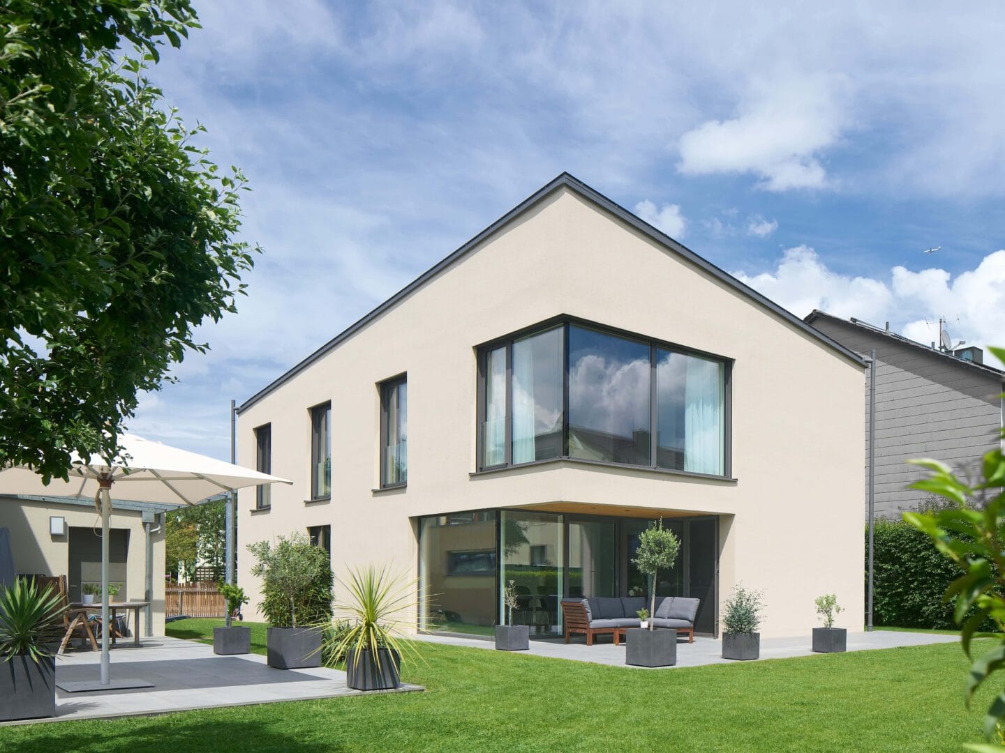 Garten und Terrasse eines modernen Einfamilienhauses mit Garage, grüner Wiese und Kübelpflanzen.