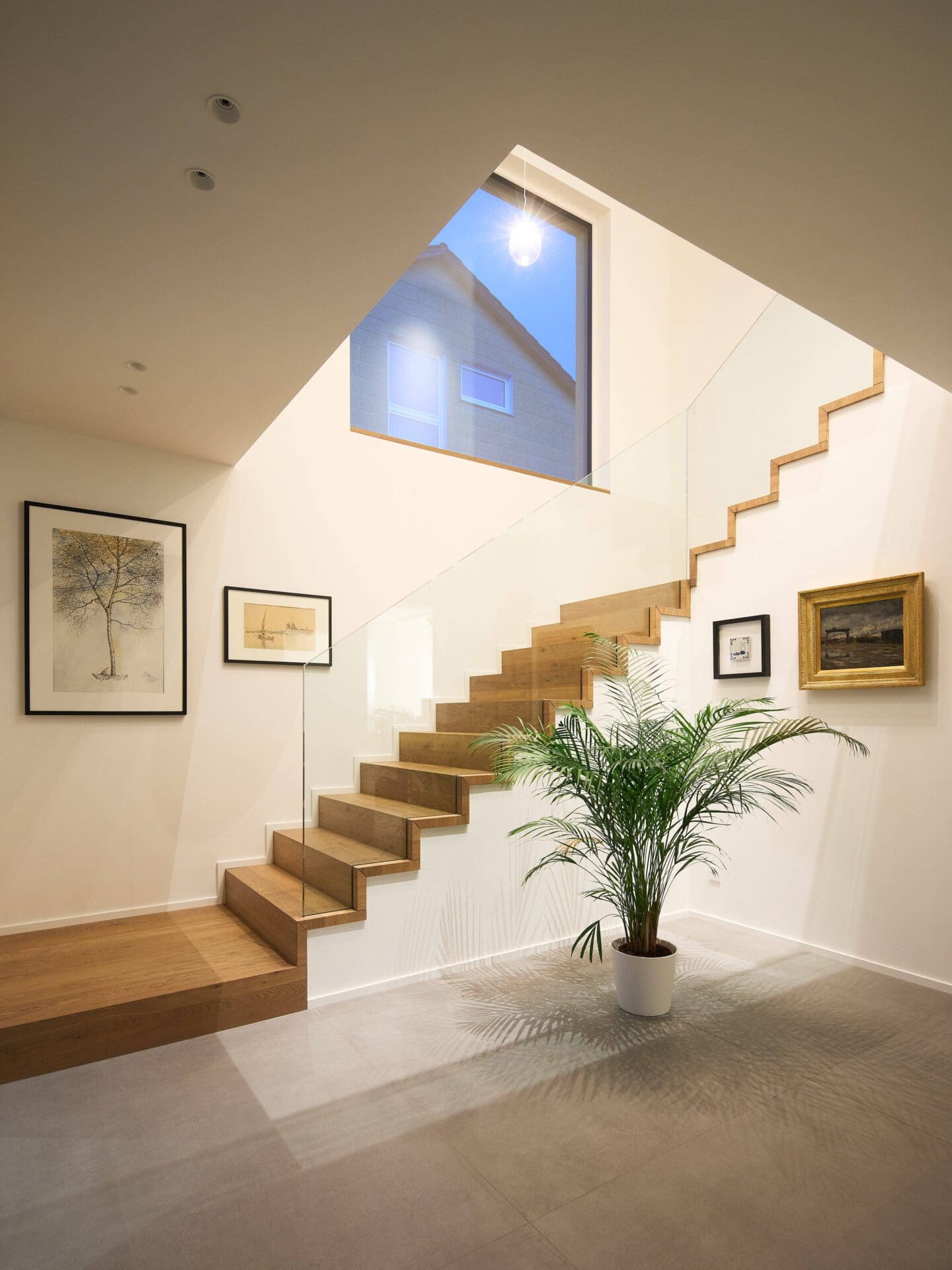 Treppenhaus eines modernen Einfamilienhauses mit Holzstufen und Glasgeländer.